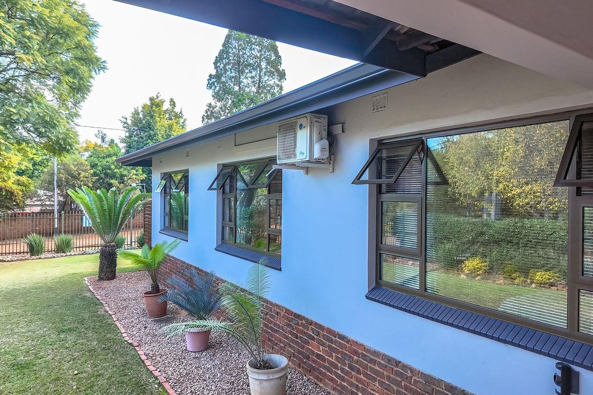 Rear exterior view of the house featuring a brick base, light-colored walls, and modern aluminium window frames with an installed air conditioning unit.