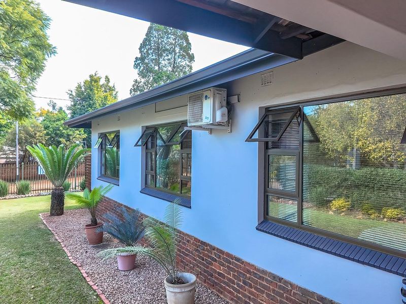Rear exterior view of the house featuring a brick base, light-colored walls, and modern aluminium window frames with an installed air conditioning unit.