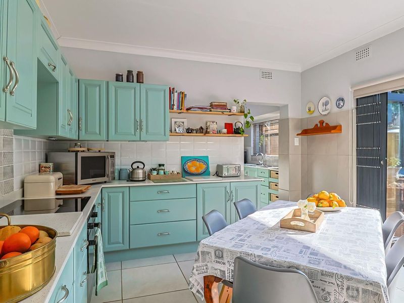 Open-plan kitchen and dining area featuring light blue cabinetry, tiled backsplash, and direct access to the rear patio through sliding glass doors.