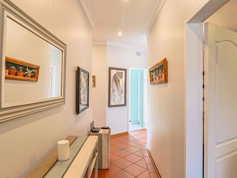 A bright hallway featuring terracotta floor tiles, coved ceilings, and recessed downlights, providing access to multiple rooms within the home.