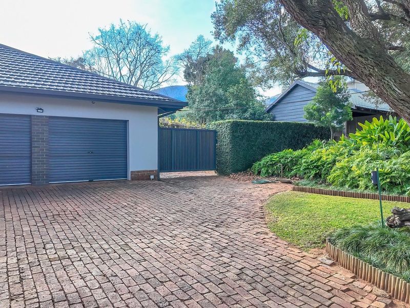Front exterior view featuring a double garage with metal doors, a brick-paved driveway, and a well-maintained landscaped garden area.