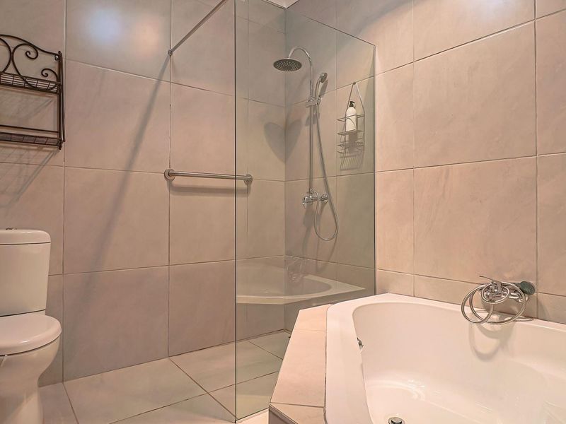 Modern bathroom featuring a built-in bathtub, a glass-enclosed shower with a rainfall shower head, and neutral wall and floor tiling.