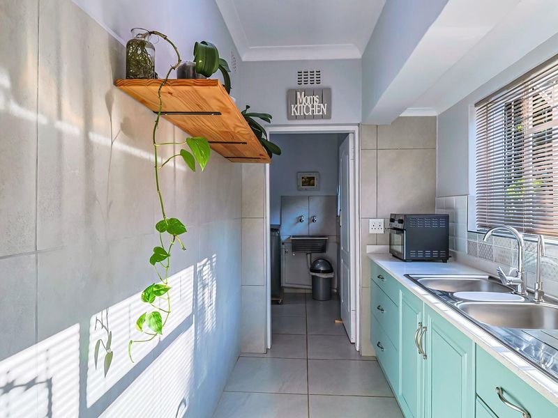 A functional scullery area featuring light blue cabinetry, a double stainless steel sink, tiled splashbacks, and a floating timber shelf.