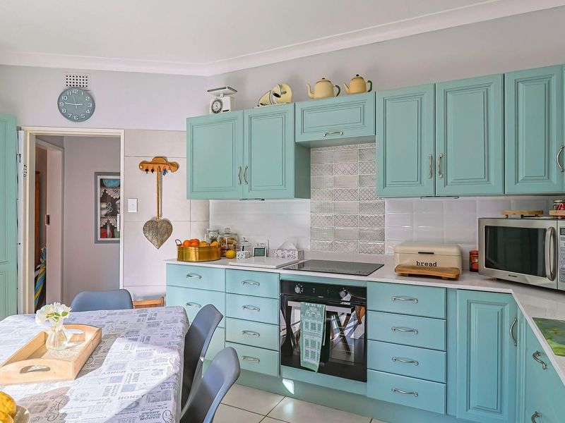 A functional kitchen featuring light blue cabinetry, stone countertops, a built-in oven, and a decorative tiled splashback.