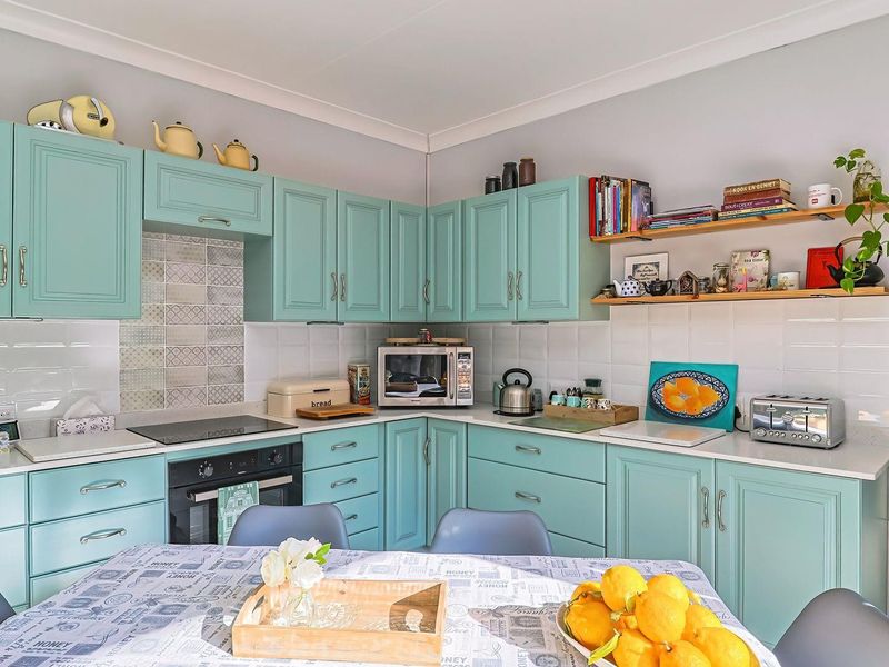 A well-maintained kitchen featuring light blue cabinetry, stone countertops, a built-in oven and hob, and decorative tiled splashbacks.