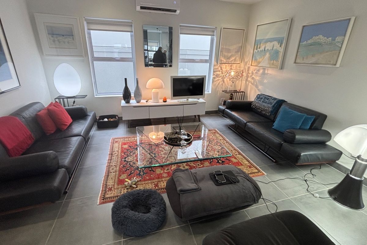 A well-maintained living room featuring large format floor tiles, a wall-mounted split-system air conditioner, and dual windows providing natural light.