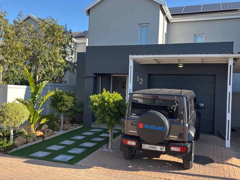 Modern double-story residential facade featuring a paved driveway, covered carport, solar panels, and a well-maintained landscaped front garden.