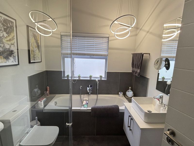 Modern bathroom featuring a built-in bathtub, glass shower screen, vessel sink vanity, and contemporary pendant lighting.