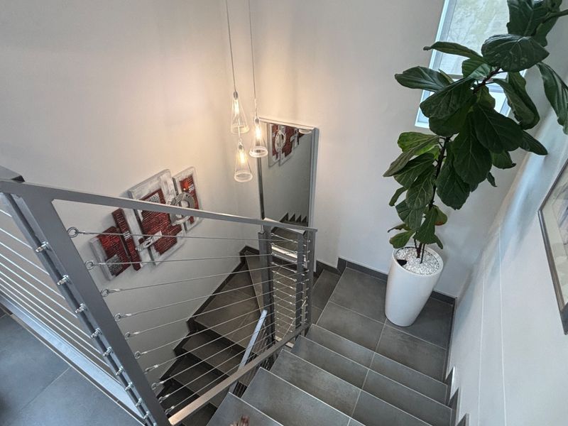 A modern staircase featuring sleek tiled steps and a contemporary stainless steel cable railing system with elegant pendant lighting.