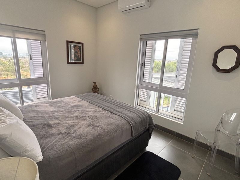 A bright, modern bedroom featuring tiled floors, split-system air conditioning, and large windows with roller blinds, offering a clean and functional living space.