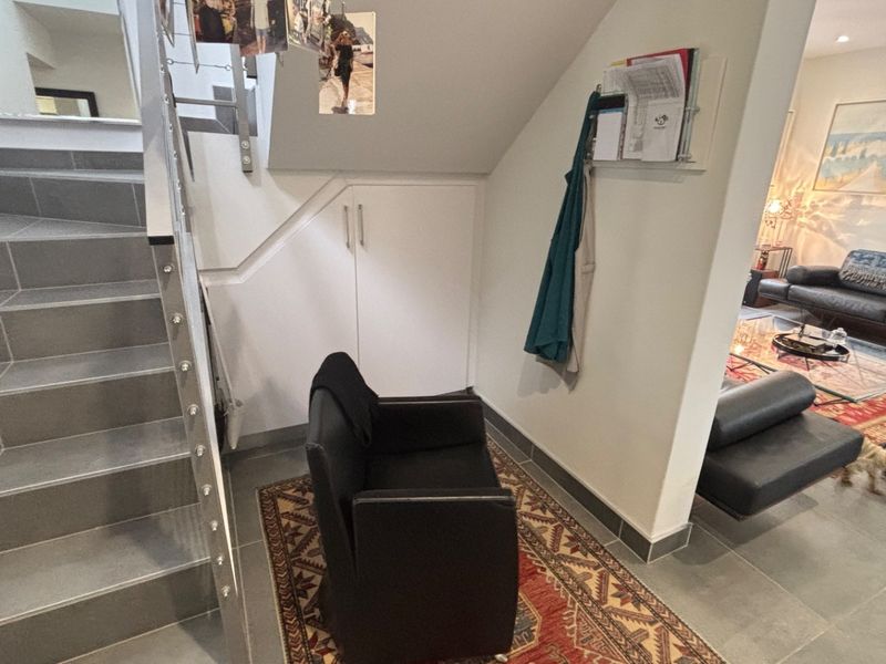 A functional hallway area featuring a tiled staircase with metal railing and convenient built-in under-stair storage cabinetry.