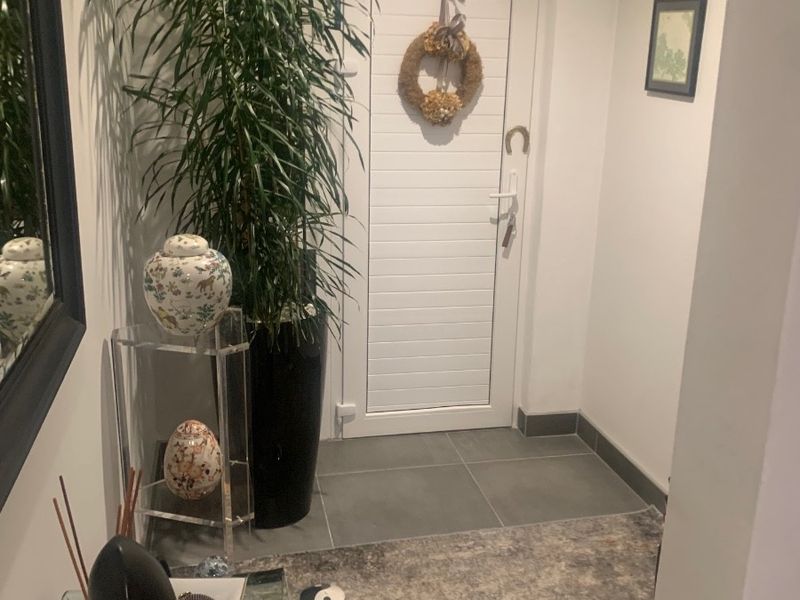 A clean and well-maintained entrance foyer featuring neutral wall finishes, tiled flooring, and a classic panelled entrance door.