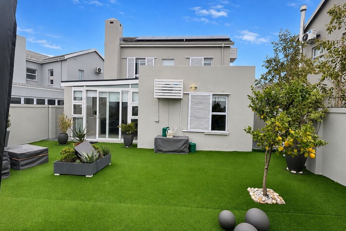 Rear view of a two-story house featuring a well-maintained artificial lawn, solar panels on the roof, and sliding glass doors leading to the interior.