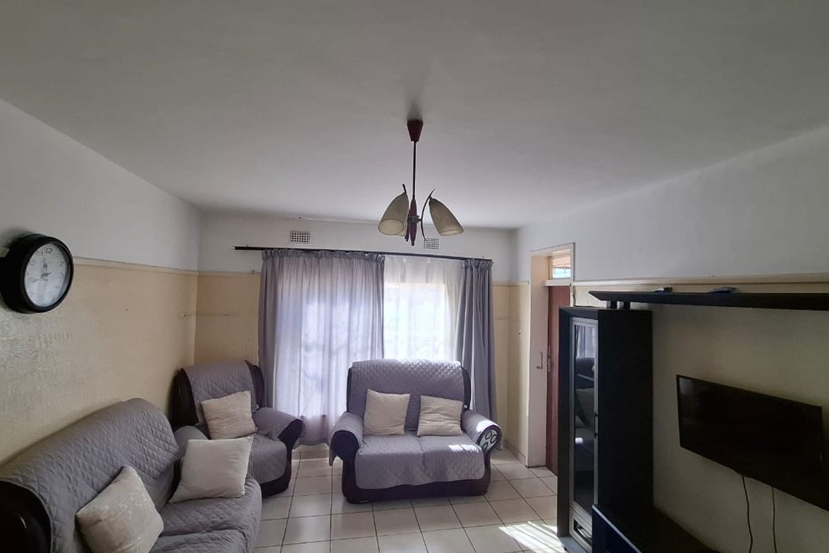 A living room featuring tiled flooring and a central ceiling light fixture, with visible wear on the wall finishes.