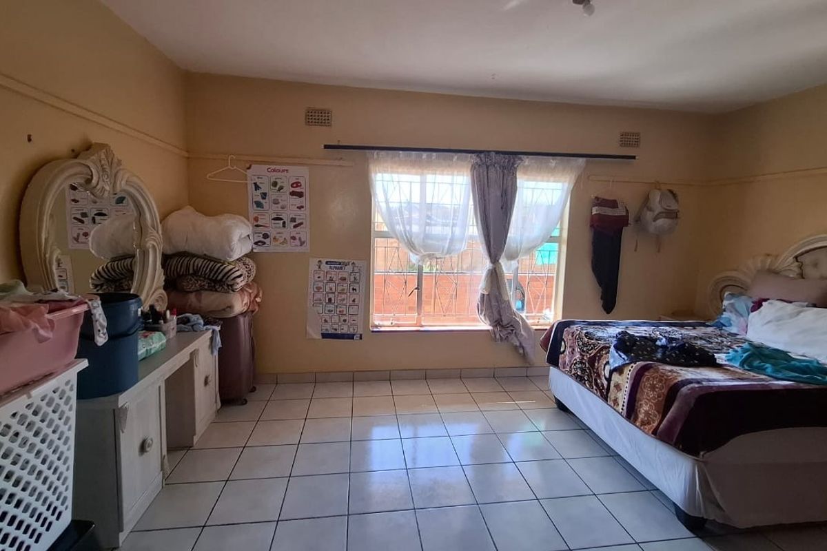A spacious bedroom featuring tiled flooring and a large window with security bars, offering a functional layout ready for cosmetic updates.