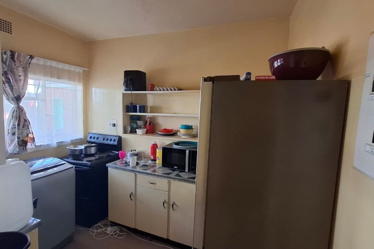 A compact kitchen area featuring dated cabinetry, a built-in extractor fan, and an exposed electrical distribution board on the wall.