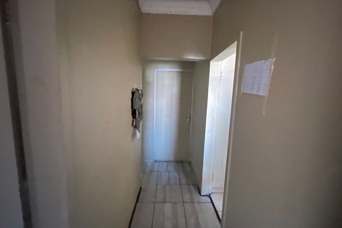 A narrow interior hallway featuring tiled flooring and decorative cornice, currently showing signs of wear and wall surface damage.
