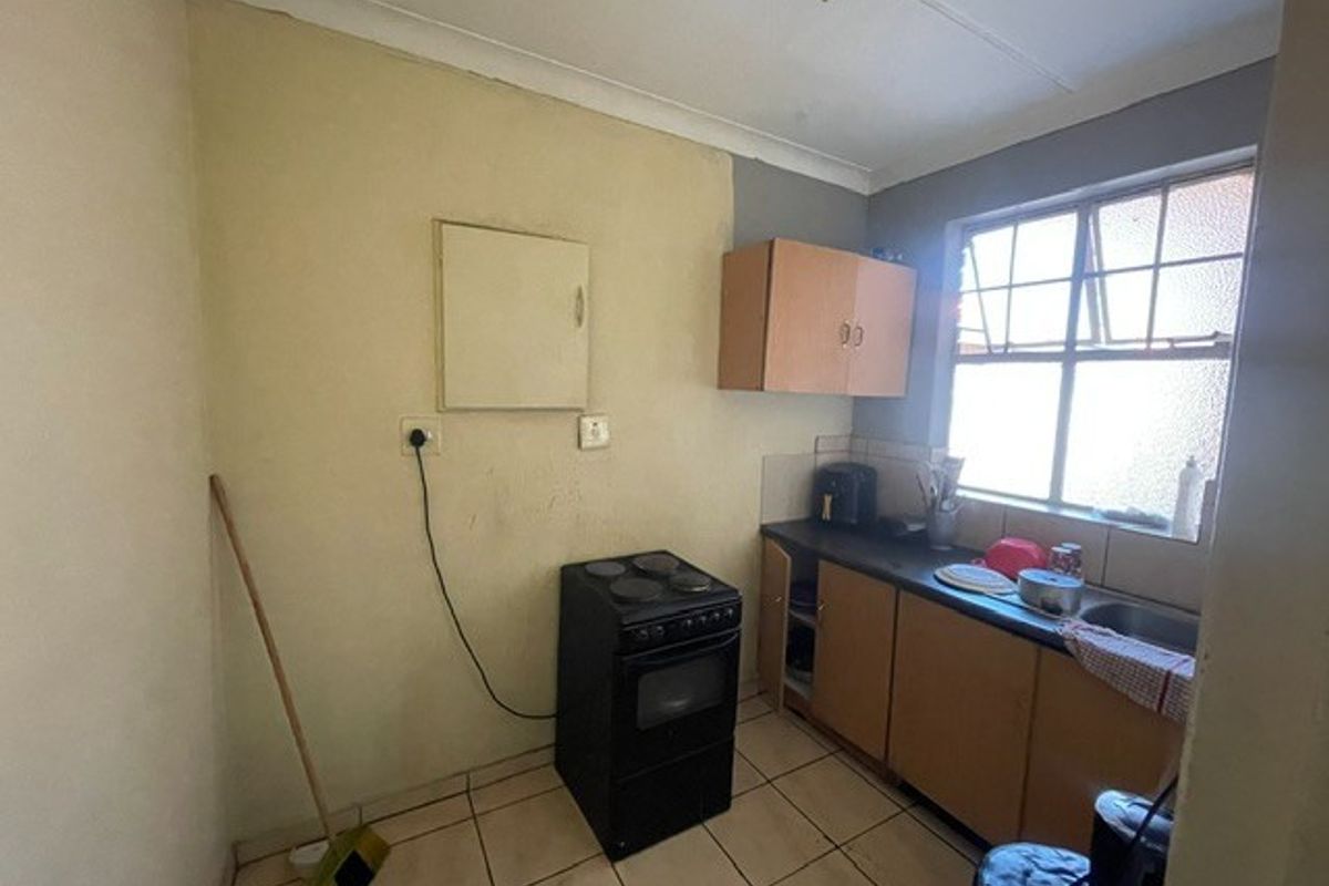 A compact kitchen featuring tiled flooring, laminate cabinetry, a stainless steel sink, and a freestanding stove, requiring cosmetic updates to improve its overall condition.