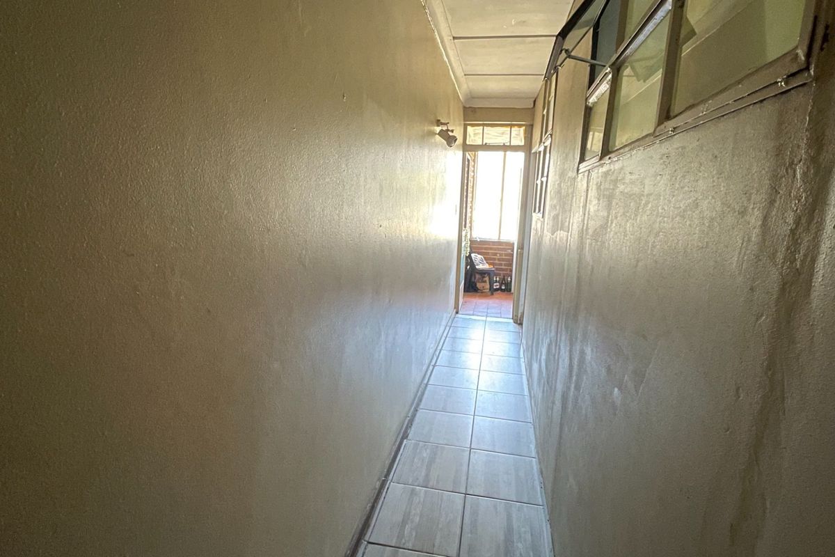 A narrow, empty hallway featuring tiled flooring and high-level windows, leading towards an exterior doorway.