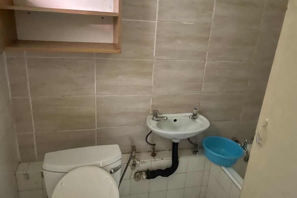 A compact bathroom featuring a toilet, wall-mounted basin, and bathtub with tiled walls. The space requires maintenance and cosmetic updates to improve its condition.