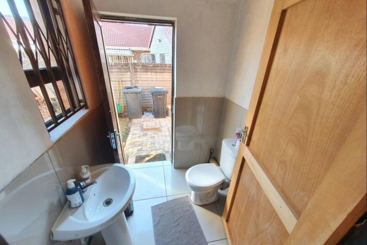 A functional bathroom featuring a pedestal basin, toilet, and tiled finishes, with direct access to the rear exterior area.