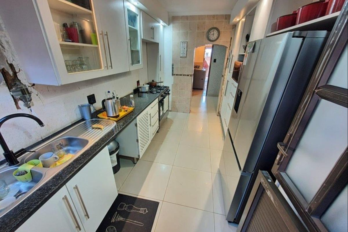 A functional galley-style kitchen featuring white cabinetry, granite countertops, a gas hob, and tiled flooring, with some visible wear to the wall finishes.