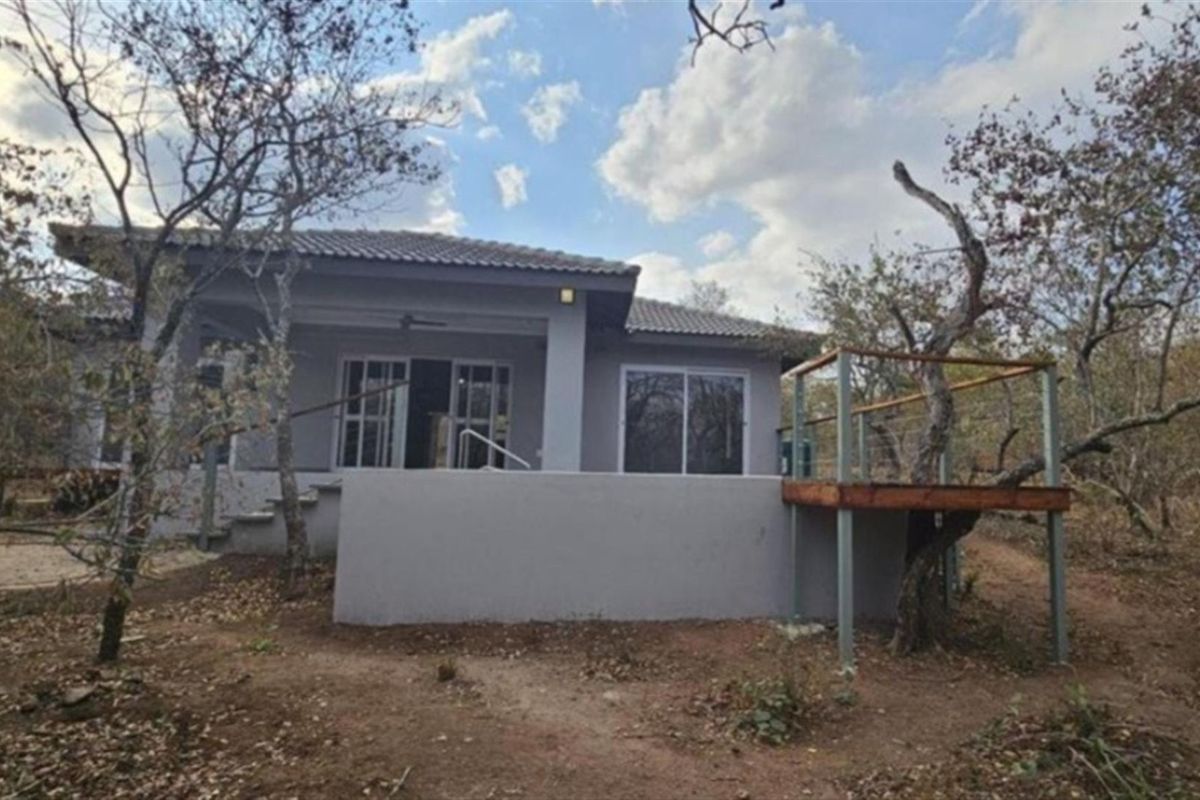 Rear view of the house featuring a covered patio, sliding glass doors, and an elevated timber deck set within a natural bushveld environment.