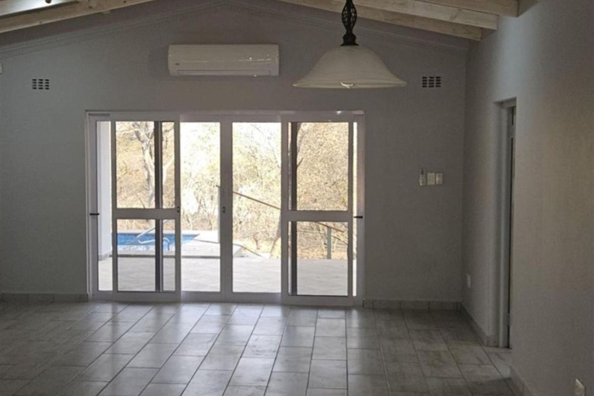 Spacious living area featuring exposed timber beams, tiled flooring, and large sliding glass doors providing direct access to the outdoor pool area.