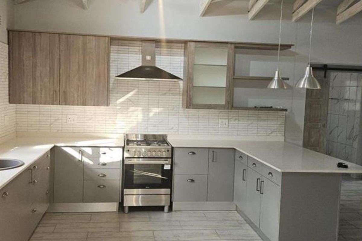 Modern kitchen featuring vaulted ceilings with exposed timber beams, stone countertops, stainless steel appliances, and contemporary tiled finishes in an open-plan layout.