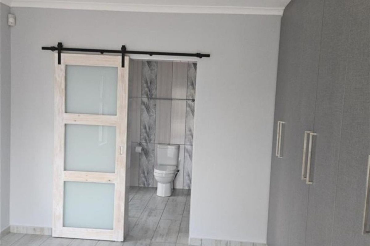A modern bedroom featuring built-in cupboards, a stylish sliding barn door, and an en-suite bathroom with contemporary tiling.