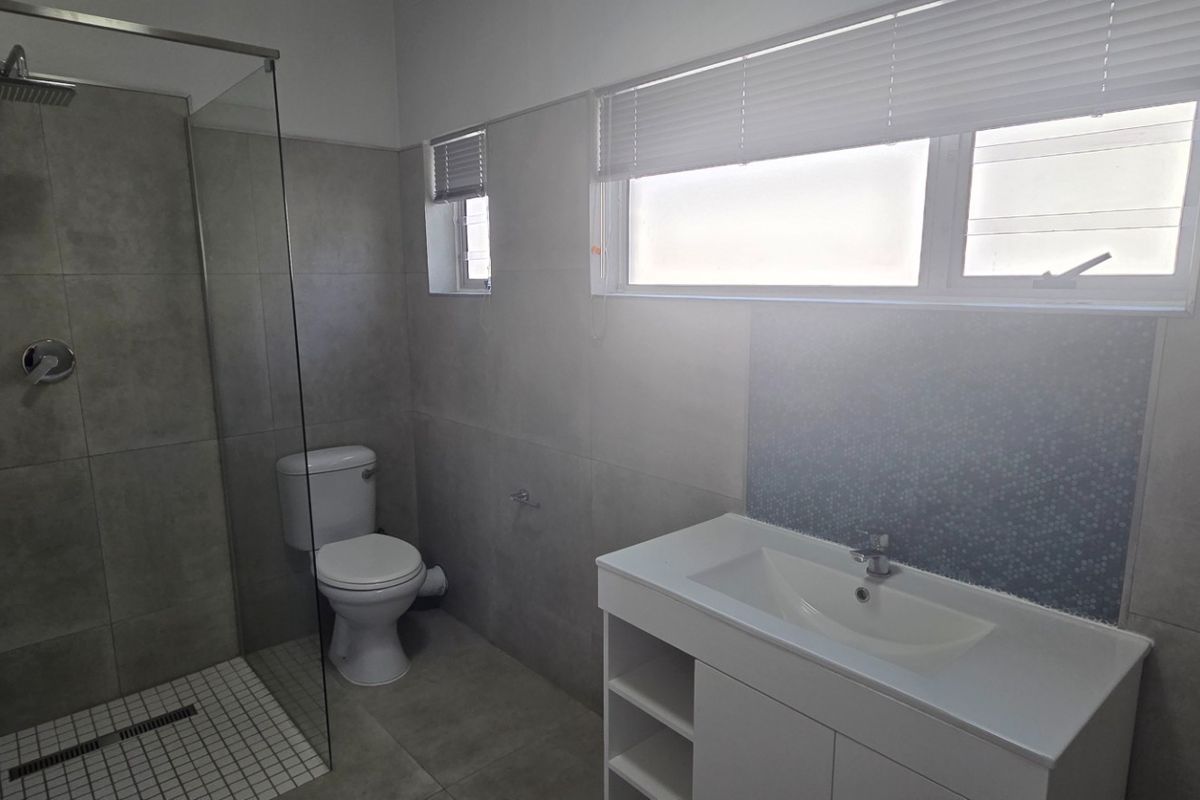 Modern bathroom featuring a spacious walk-in shower with glass screen, contemporary vanity unit, and neutral floor-to-ceiling tiling.