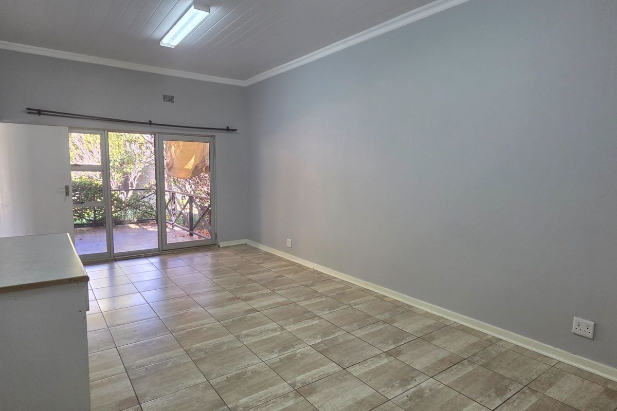 A spacious, empty living area featuring neutral tiled flooring, coved cornicing, and sliding glass doors that provide access to an outdoor patio space.