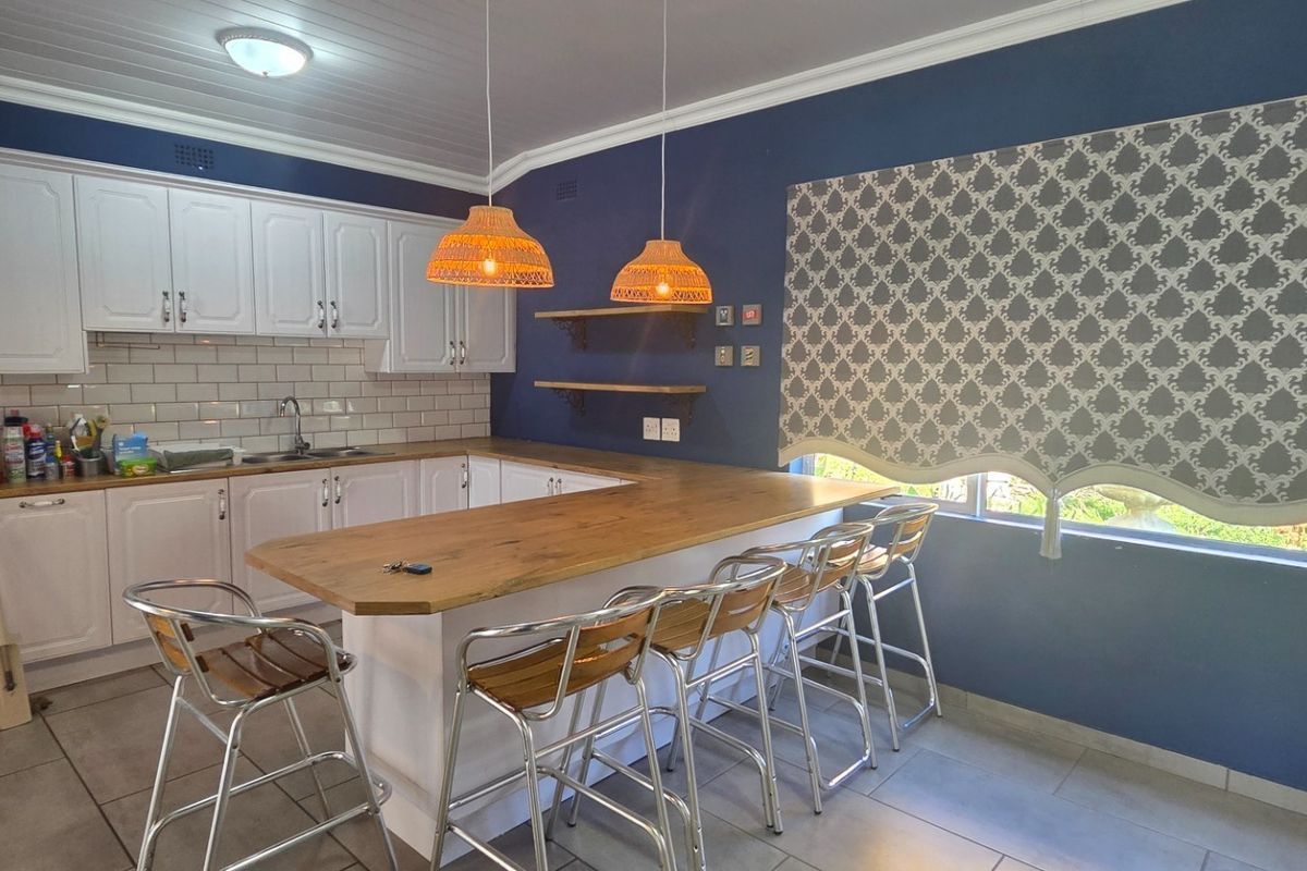 A well-maintained kitchen featuring white cabinetry, a wooden breakfast bar, subway tile backsplash, and tiled flooring with a modern blue accent wall.