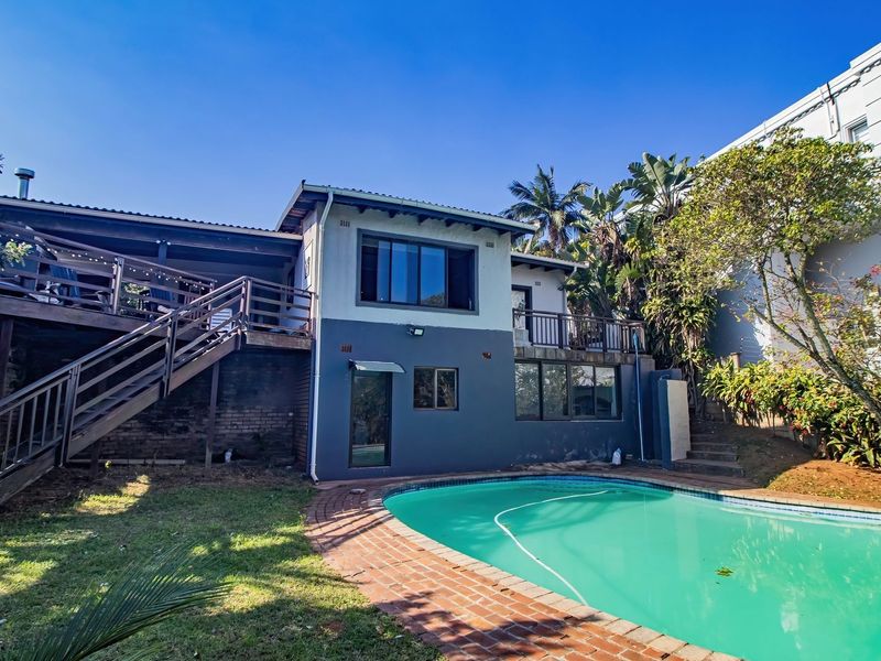 Rear view of the property featuring a swimming pool, brick paving, and a raised wooden deck with an external staircase leading to the upper level.