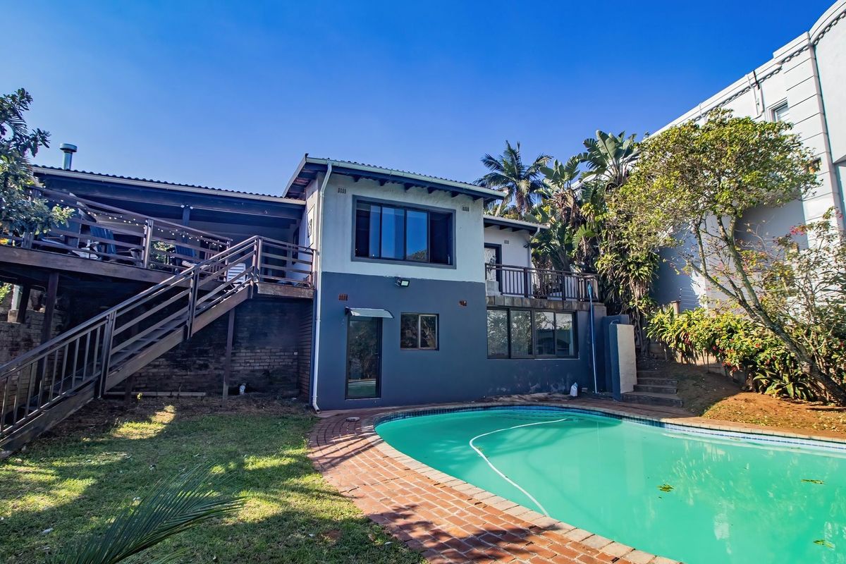 Rear view of the property featuring a swimming pool, brick paving, and a raised wooden deck with an external staircase leading to the upper level.