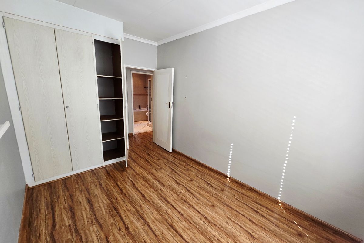 A vacant bedroom featuring laminate flooring, a built-in wardrobe, and direct access to an adjoining bathroom.