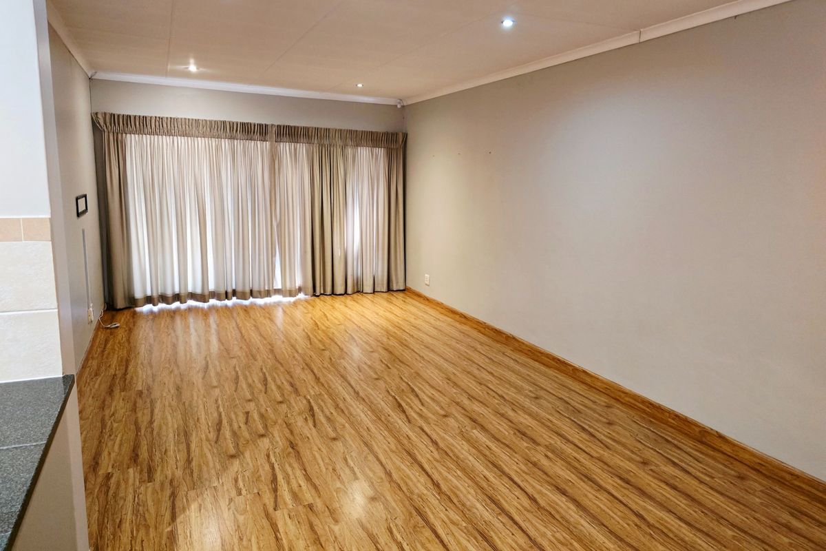 A spacious, empty living area featuring warm-toned laminate flooring, recessed downlighting, and full-length curtain tracks, offering a clean and neutral canvas.