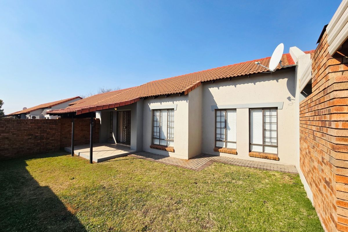 Rear view of the townhouse featuring a private garden, covered patio area, and secure brick boundary walls.