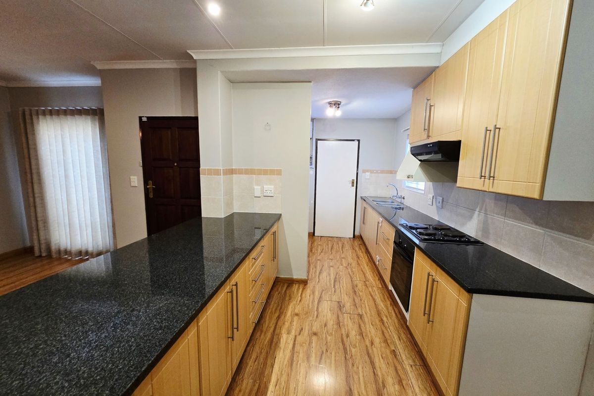 A functional kitchen featuring light wood cabinetry, dark granite countertops, a gas hob, and integrated appliances, finished with laminate flooring.