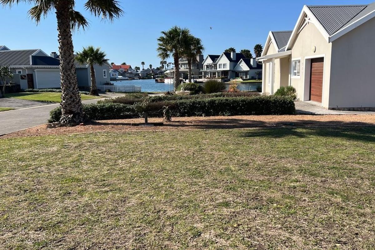 A scenic view of a residential waterfront property featuring a well-maintained garden, palm trees, and clear access to the canal.