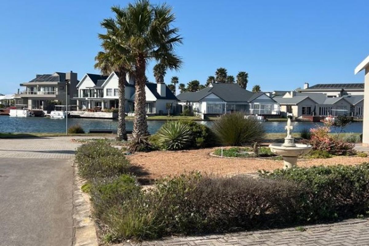 A scenic view of a landscaped garden with a water feature, overlooking a tranquil canal and surrounding residential properties.