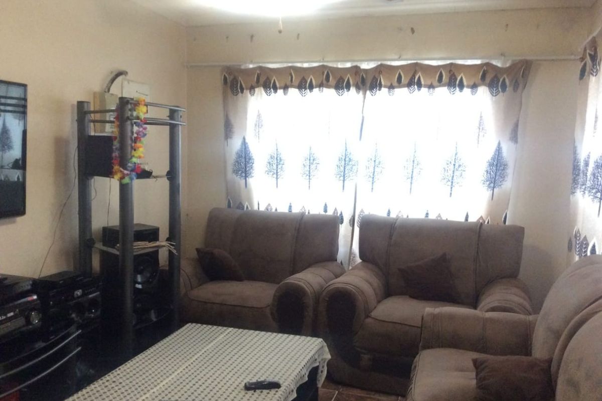 A living room featuring tiled flooring and a ceiling fan, currently showing signs of wear including peeling paint and exposed wiring.