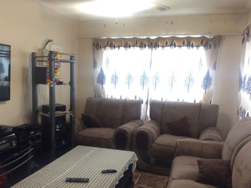 A living room featuring tiled flooring and a ceiling fan, currently showing signs of wear including peeling paint and exposed wiring.