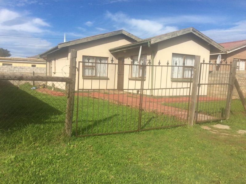 Front view of a single-story detached house featuring a metal security gate, wire fencing, and a paved walkway leading to the entrance.