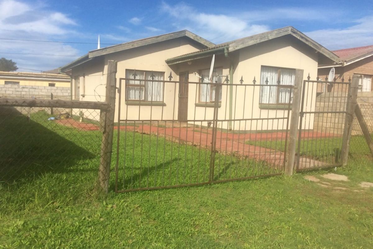 Front view of a single-story detached house featuring a metal security gate, wire fencing, and a paved walkway leading to the entrance.