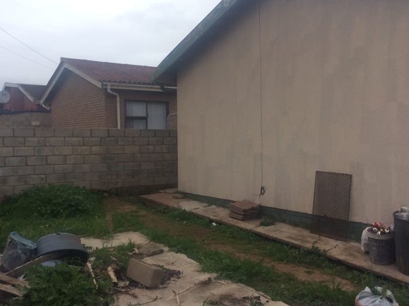 Rear exterior view of the property showing a concrete boundary wall, paved pathway, and plastered exterior wall with exposed wiring.