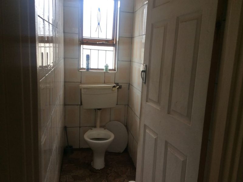 A small, dated bathroom featuring tiled walls and floor, equipped with a standard toilet and a window with security bars.