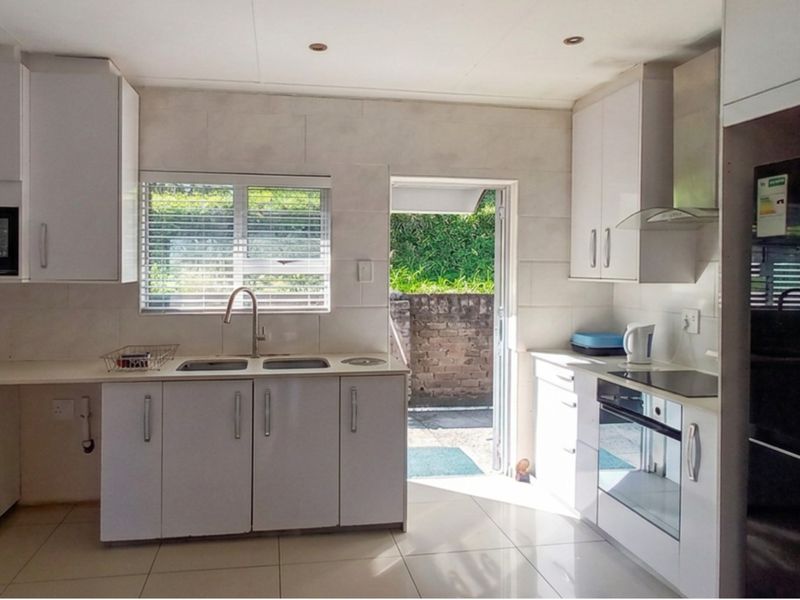 A clean, modern kitchen featuring white cabinetry, integrated appliances, tiled finishes, and direct access to an outdoor area.