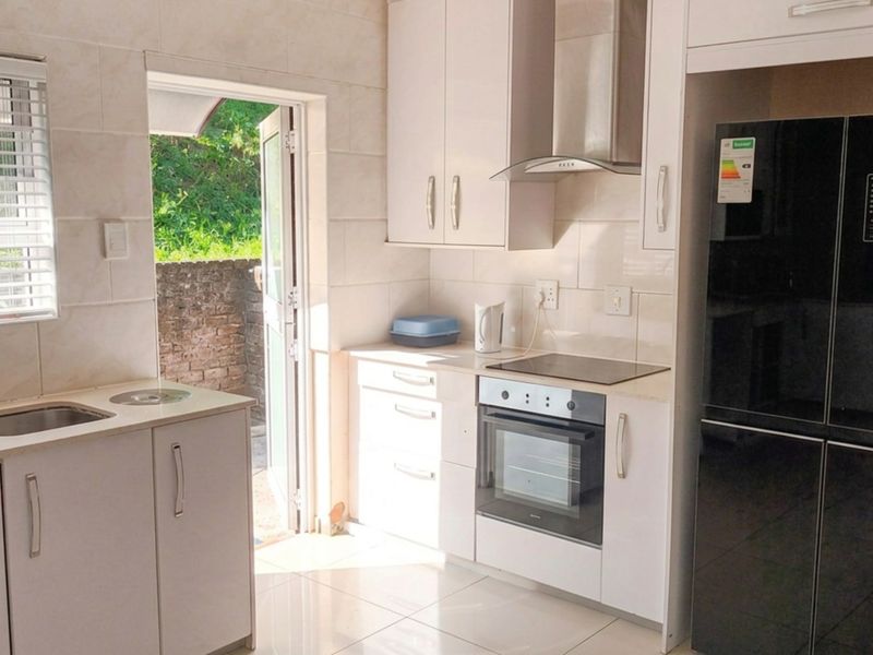 Modern kitchen featuring white cabinetry, integrated appliances including an oven and hob, tiled splashbacks, and direct access to an outdoor area.