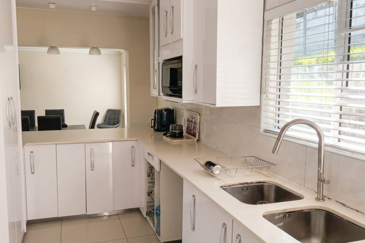 Modern kitchen featuring white gloss cabinetry, stone countertops, double stainless steel sink, and built-in microwave, with an open-plan flow to the dining area.